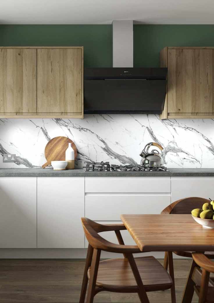 Green kitchen with marble splashback and light wooden cupboards, dark wooden flooring and dining table