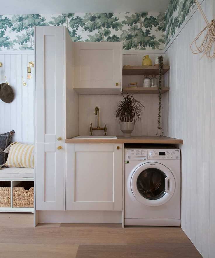 A neutral laundry room with green and white wallpaper on top quarter of walls with tall white vertical paneling, and an entryway bench to the left which is part of a boot room