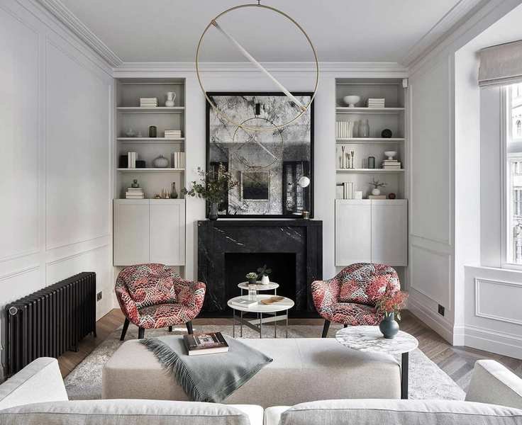 A small living room with white walls, pink arm chairs and shelving on either side of a black marble fireplace.