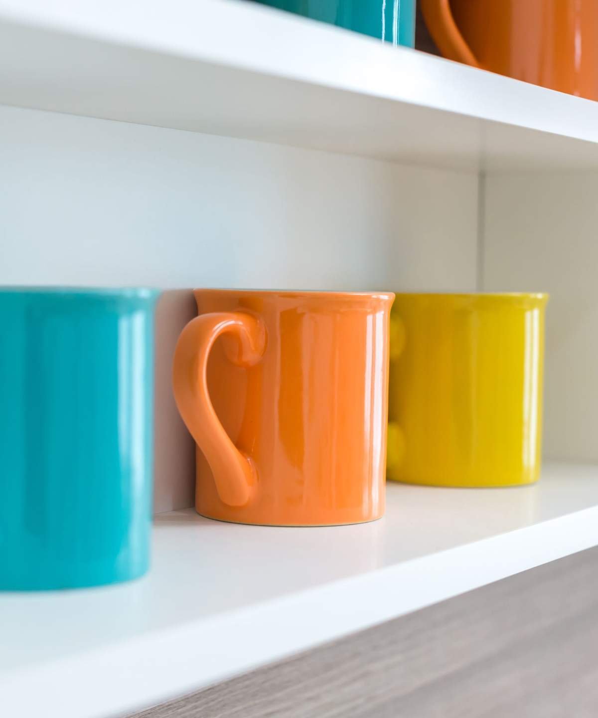 A blue, orange, and yellow coffee mug lined up on a white shelf