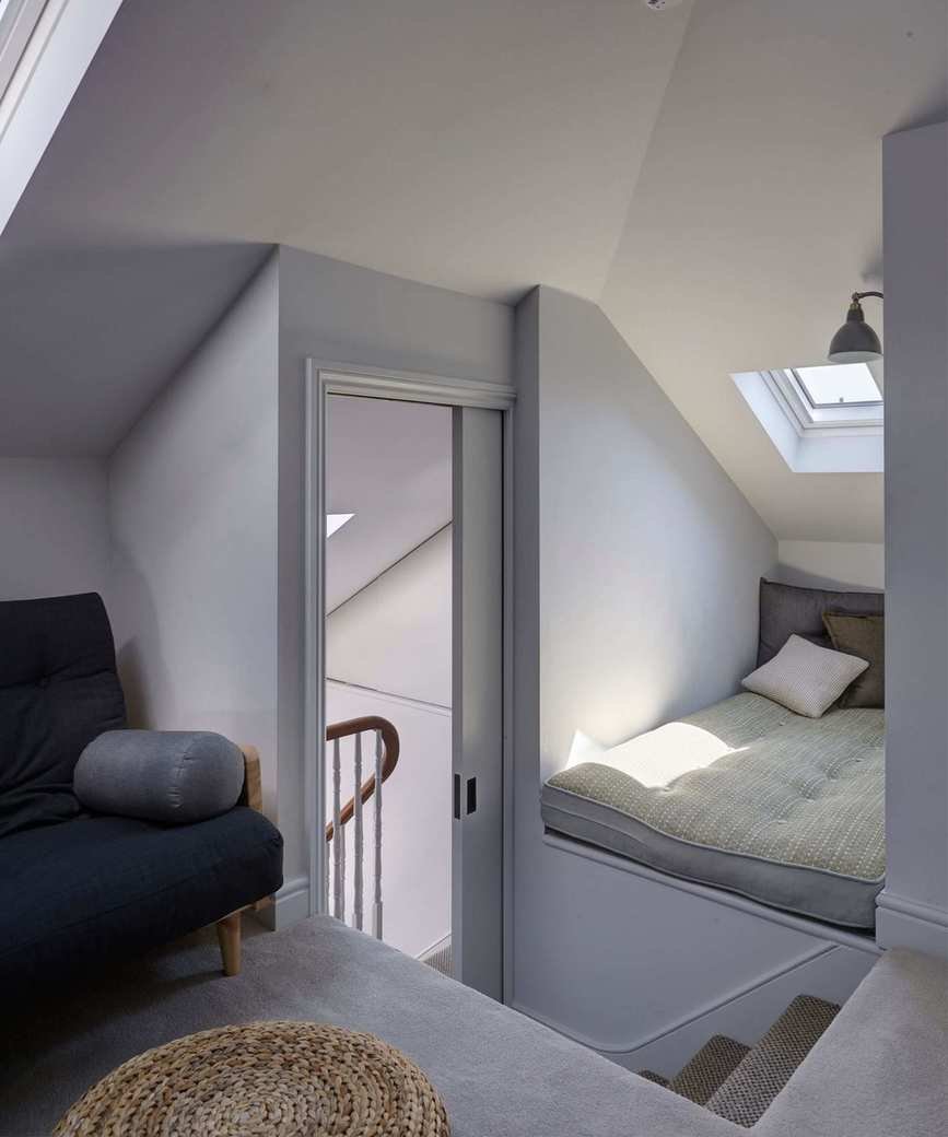 A bright attic space with a sliding door, futon mattress, blue upholstered chair and rattan stool