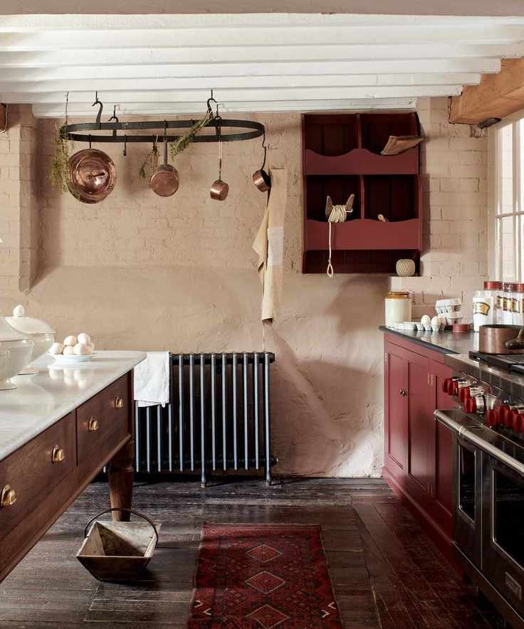 A country kitchen with deep pink cabinets, a wooden freestanding island, and a wall-mounted veg box for storage