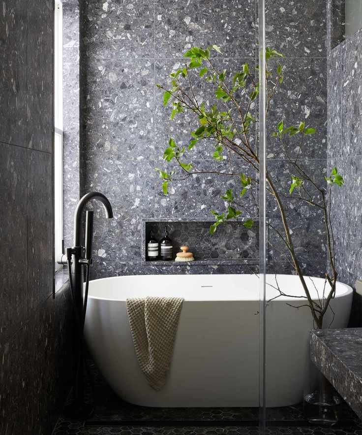 A small bathroom with gray terrazzo tiles and a freestanding tub.