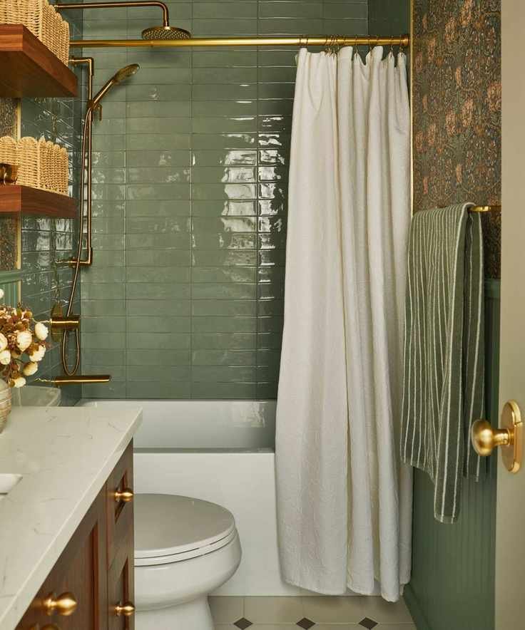 a sage green tiled bathroom with pink and green floral wallpaper, a wooden vanity, bath, and floating shelves