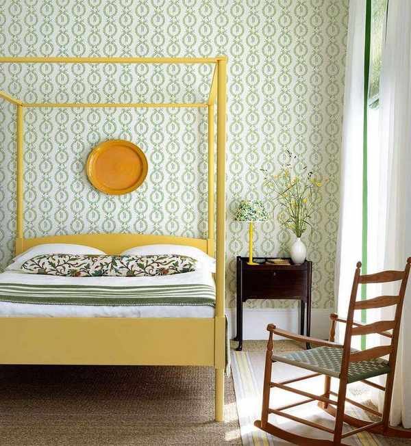 A yellow four-poster bed in front of a wall with green and white patterned wallpaper