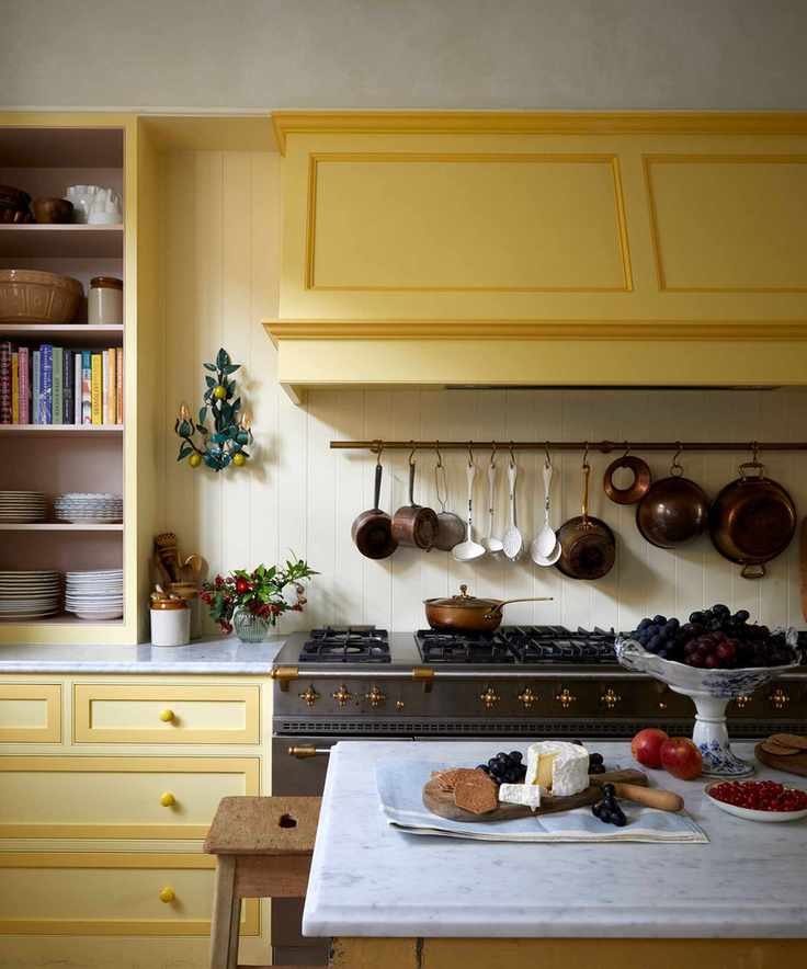 Kitchen with yellow units, cream walls, parquet flooring and large range cooker with saucepans hanging on the wall above.