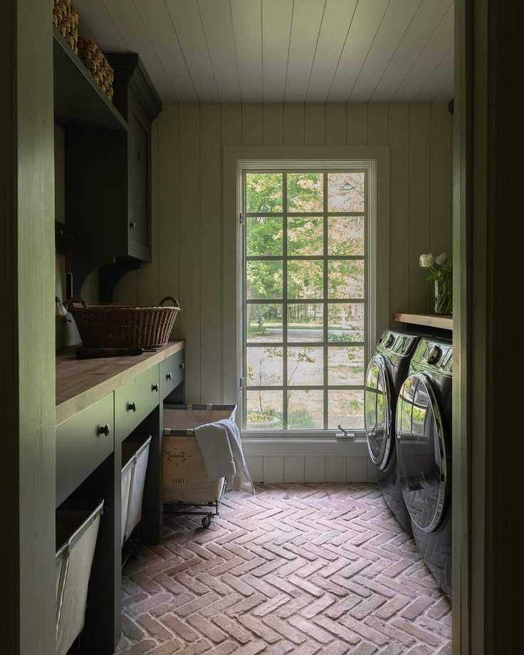 House Seven Design Laundry Room with dark cabinetry. terracotta floor and laundry carts under countertop