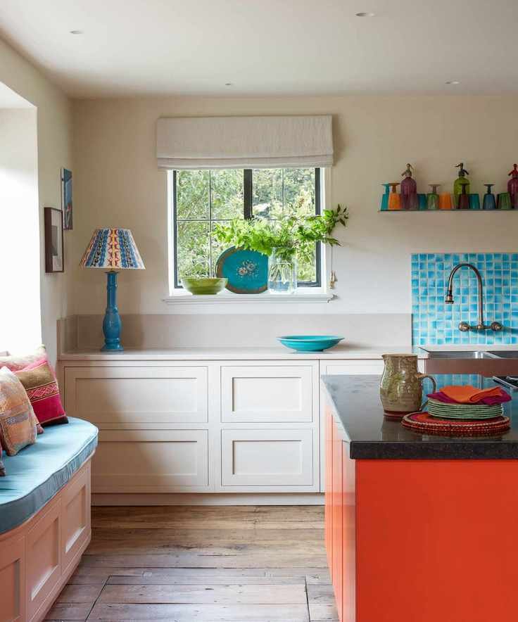 Colorful kitchen with dark wooden flooring, red kitchen island, blue tiles and accessories, cream painted walls and cabinetry