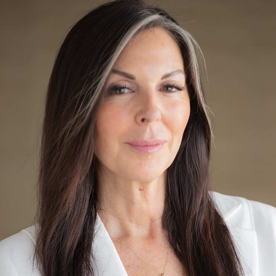 a headshot photo of psychotherapist Shari B. Kaplan: a brown haired lady in a white shirt against a light brown background
