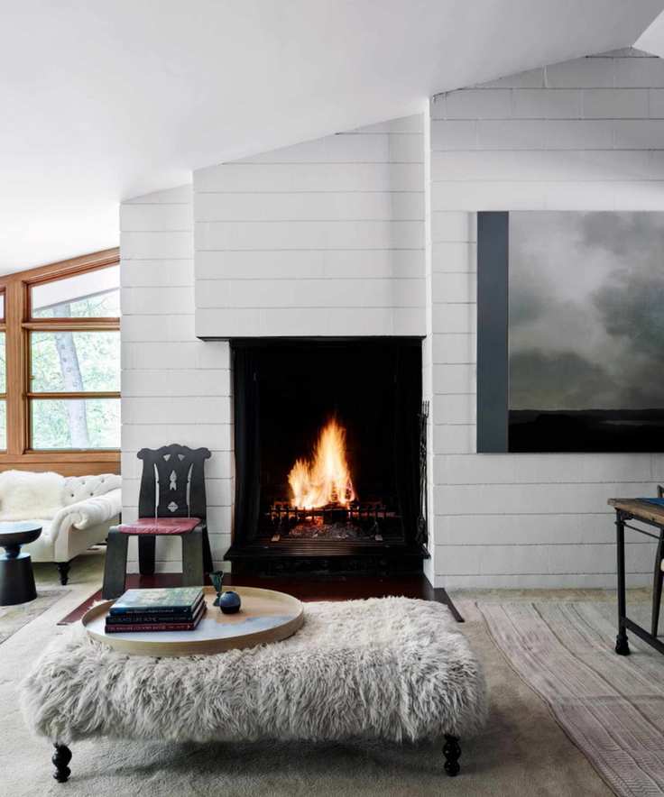 Midcentury living room with white wood panelling, fireplace, shaggy fur stool, wood chair and white sofa