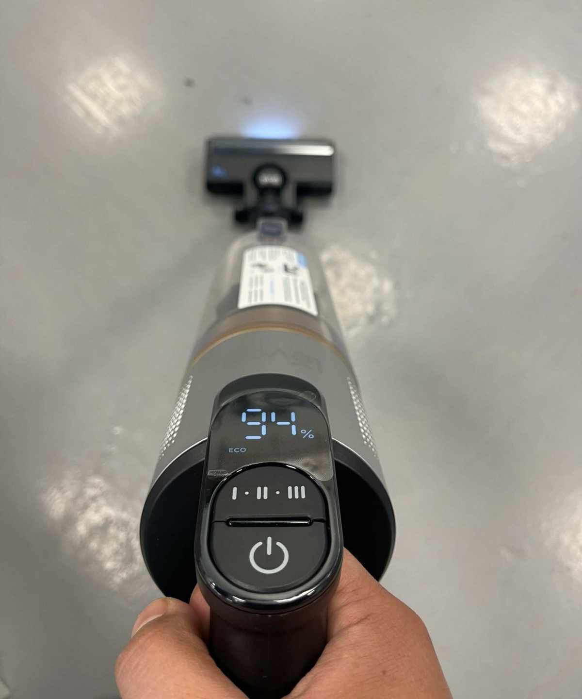Closeup of the Levoit LVAC-300 cordless vacuum cleaner from above, showing the power button, suction mode button, and screen showing battery life and ECO mode in testing center.