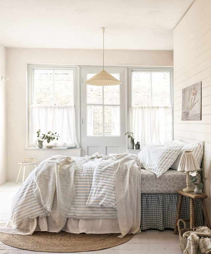 fisherman aesthetic bedroom with a layered bed with a gingham bed skirt, striped bedding, floral sheets and shiplap bedroom walls