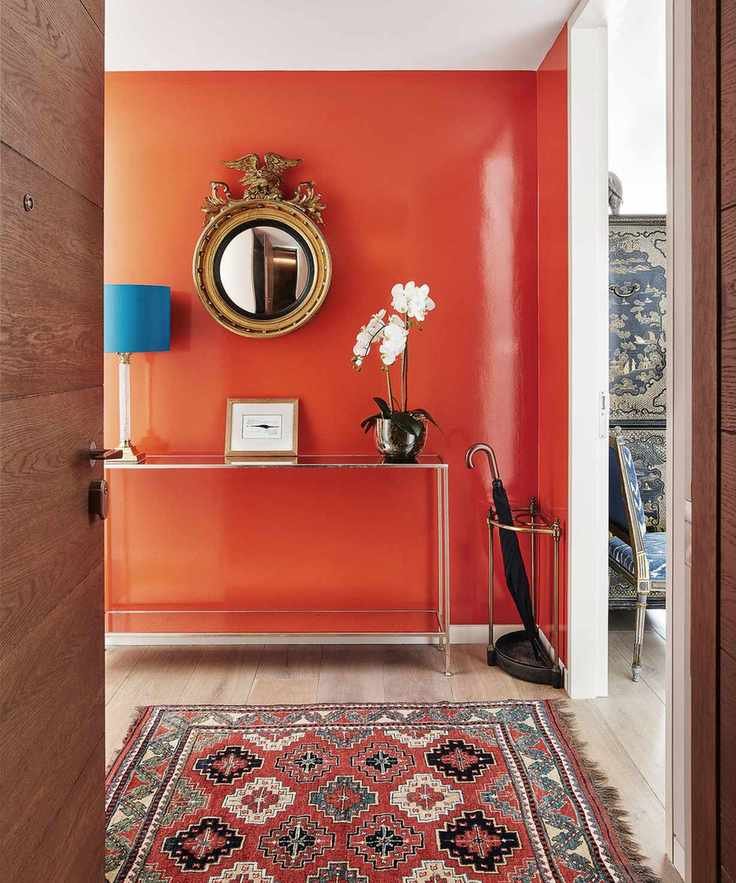 Hallway with a wall painted a bright orange with a matching rug, metallic console table, and a round mirror