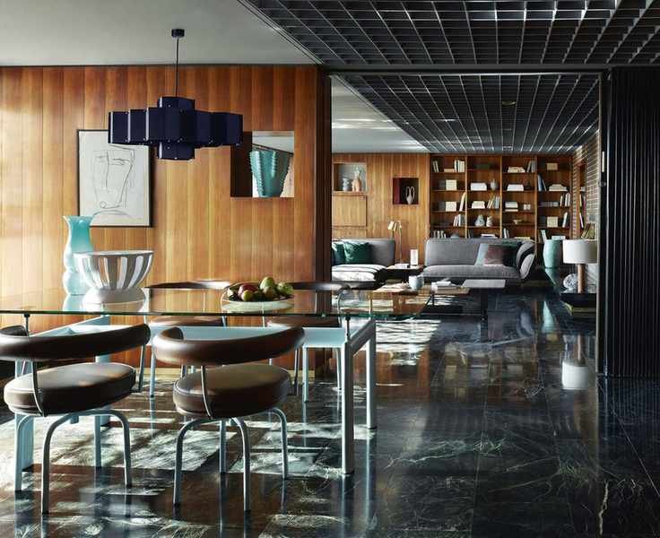 Glass dining table with blue legs and leather dining chairs in dining room with wooden walls