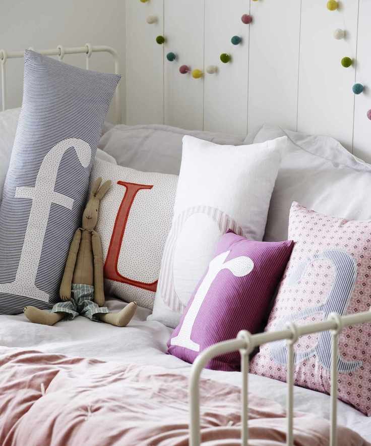 Girls' bedroom decor in a white scheme with a selection of pastel colored cushions on a child's daybed, each embroidered with a letter and spelling out the name 'Flora'