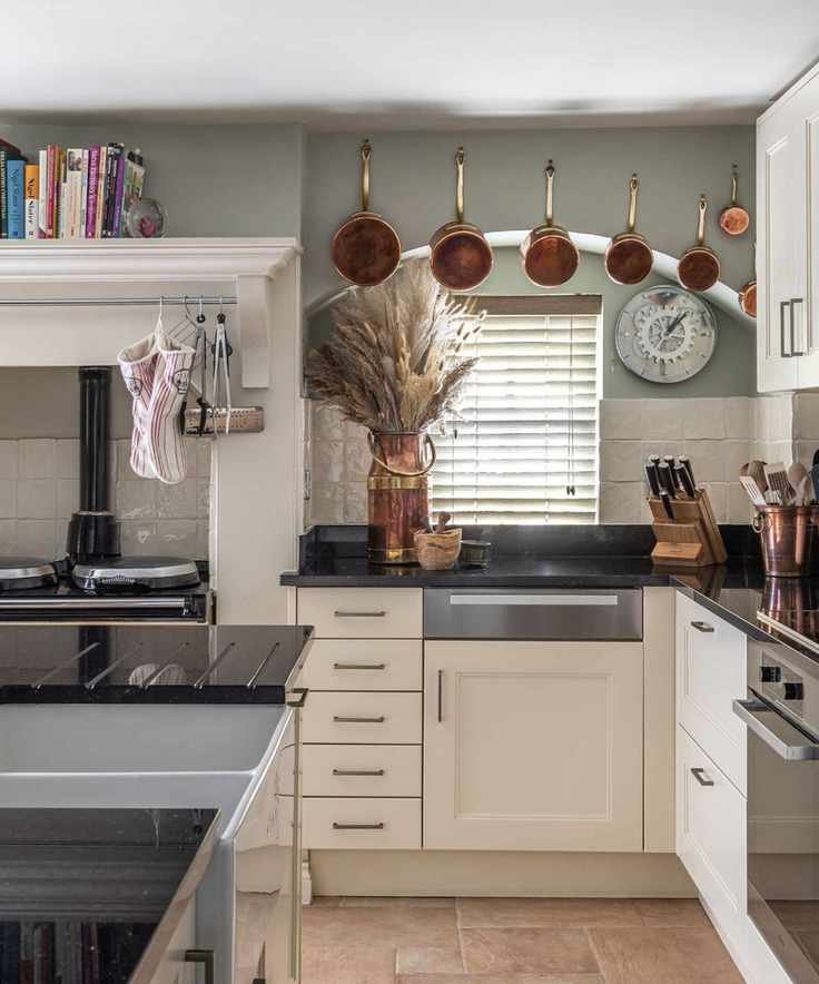 Country style kitchen with cream cabinets hooks above sink for hanging copper pots and tall shelving for cookbooks above range alcove
