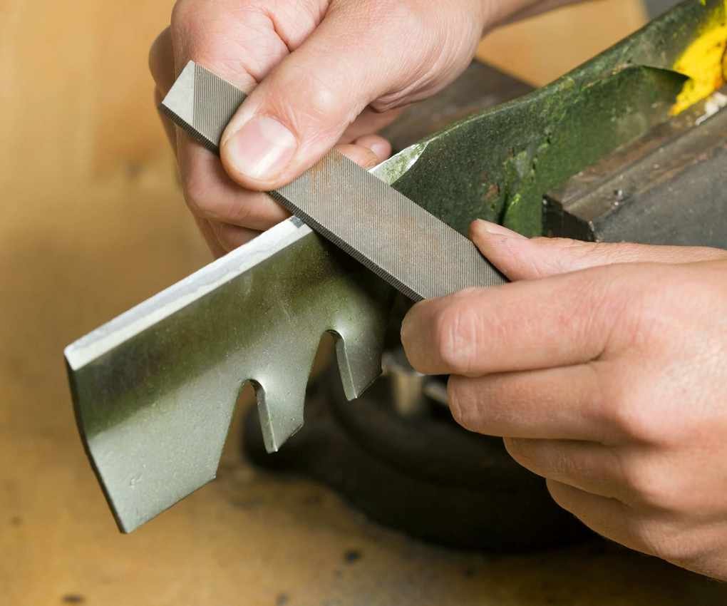 A close up on hands sharpening lawn mower blades with a file