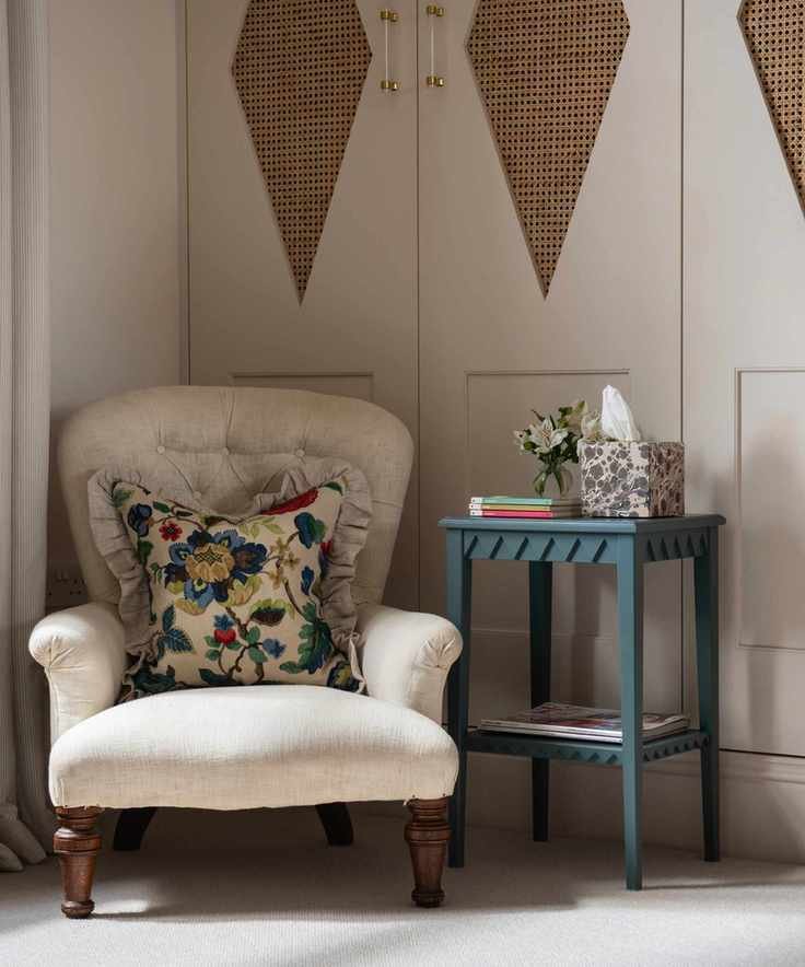 bedroom with fitted wardrobes in taupe, plain upholstered armchair with floral couch pillow, blue side table, Georgie Wykeham Designs