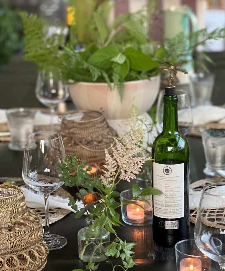 table set with rattan placemats, glassware and greenery in a central bowl and small glass vases