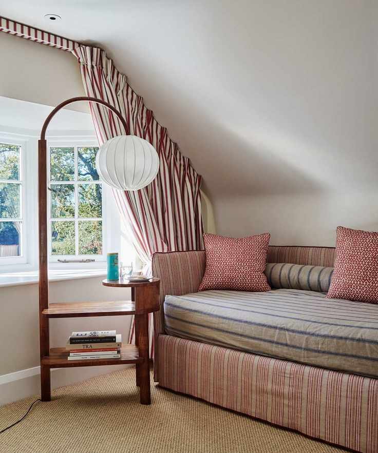 A white attic space with striped curtains, a striped sofa, and a brown floor lamp with a white lampshade in front of bay windows.