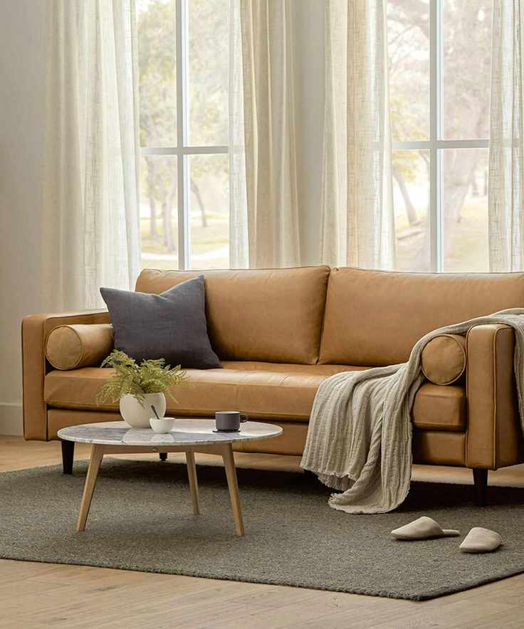 leather couch in a neutral living room with a grey rug and marble and wood round coffee table