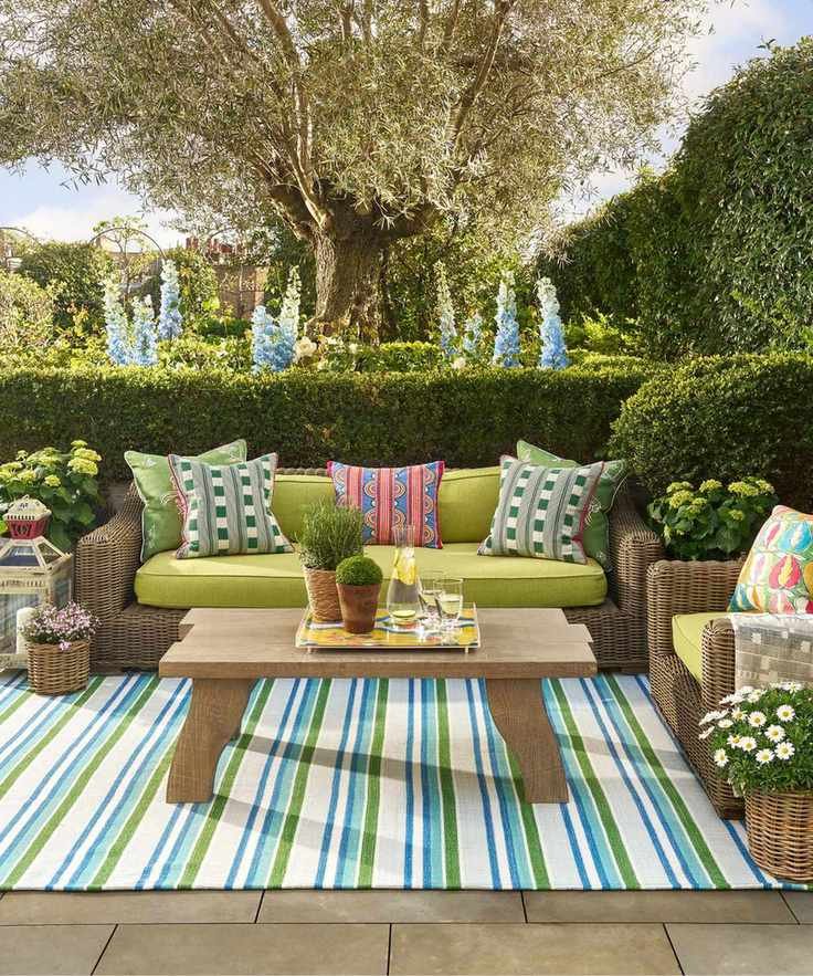 outdoor living room area with a blue and green striped rug, wooden coffee table, wicker sofas with green cushions and patterned throw pillows