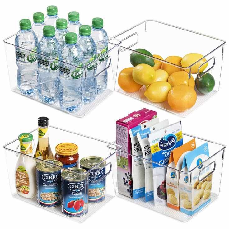 Four clear plastic freezer bins with integrated handles filled with water bottles, citrus fruits, tins, bottles, jars, and cardboard boxes