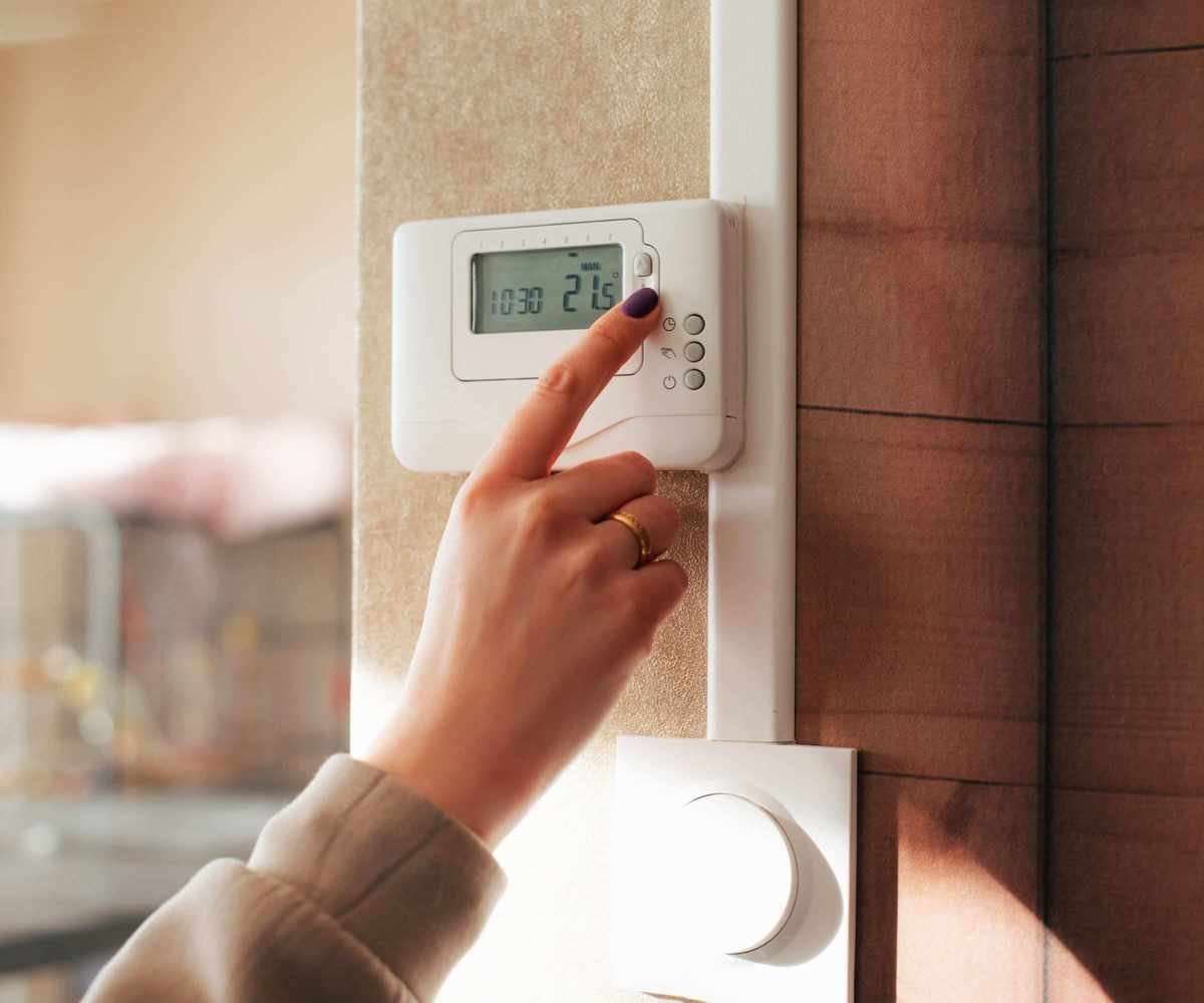 someone adjusting a wall mounted thermostat