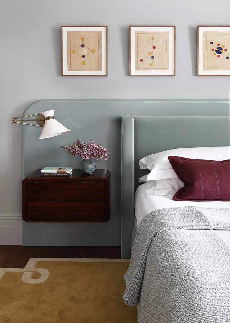 A bedroom with a light blue glass feature behind the bed, a blue velvet headboard, and a floating wooden nightstand