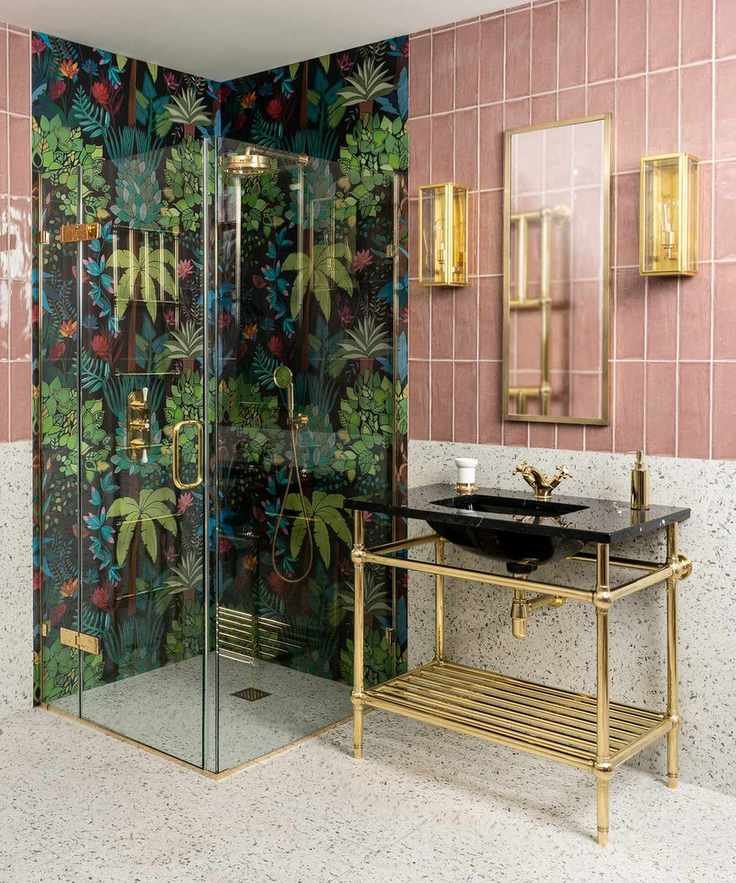 An example of bathroom shelf ideas showing a pink-tiled bathroom with walk-in shower clad with tropical patterned wallpaper, and an open gold vanity unit
