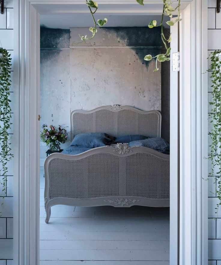 View through a doorway from the bathroom into the master bedroom with white wooden floorboards, blue stained walls, and French cane bed.