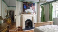 a large bedroom with a victorian fireplace, green and white striped walls with alcove closets with mirror fronts