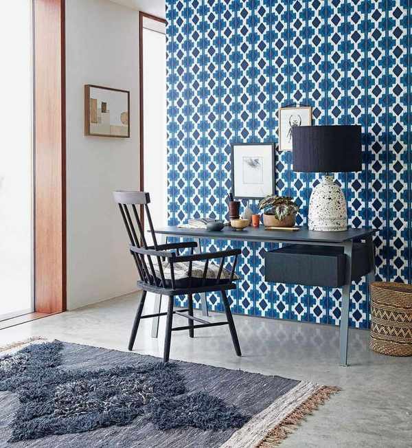 A home office with feature wall papered in a geometric pattern, with tiled floor and rug, desk and armchair.