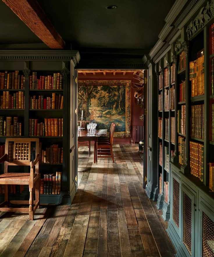 A dark-toned library with floor-to-ceiling green bookshelves filled with leather-bound books, leading into a formal dining room with a large wall tapestry and a wooden table