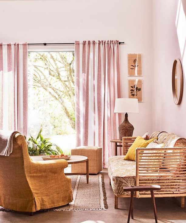 A living room with pink curtains and walls, a couch and armchair, a wooden coffee table, and a lamp.